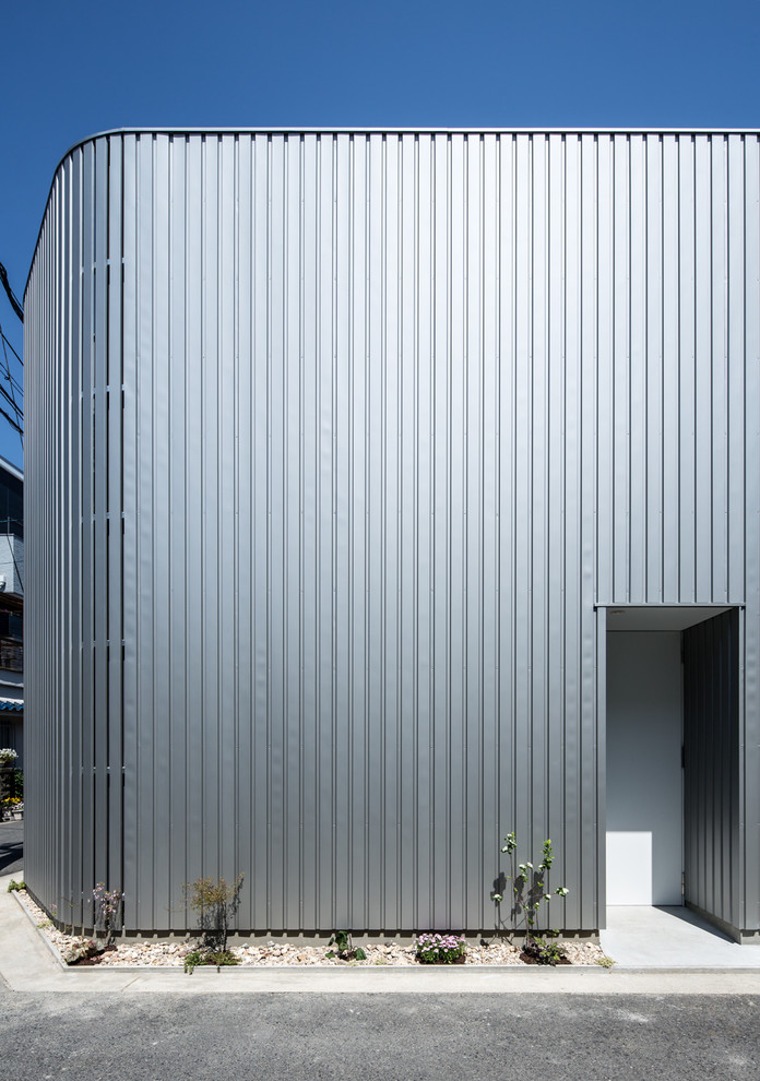 Mittelgroßes, Zweistöckiges Modernes Einfamilienhaus mit Metallfassade, grauer Fassadenfarbe, Flachdach und Blechdach in Osaka