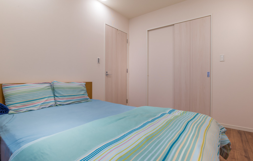 Imagen de dormitorio principal nórdico de tamaño medio sin chimenea con paredes blancas, suelo de contrachapado y suelo marrón
