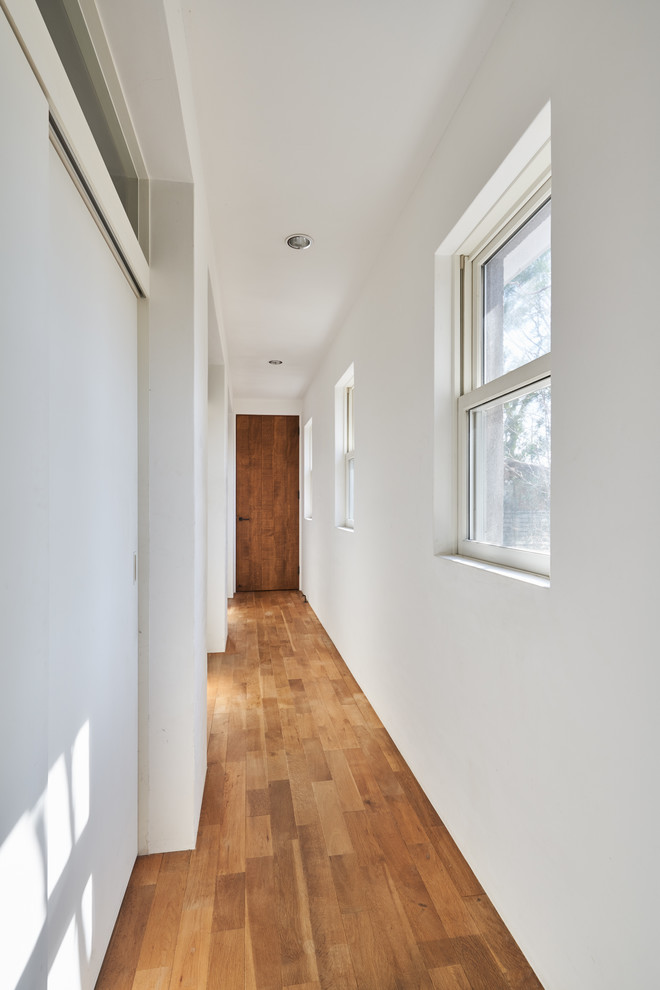 Esempio di un ingresso o corridoio minimalista di medie dimensioni con pareti bianche, pavimento in legno massello medio e pavimento marrone