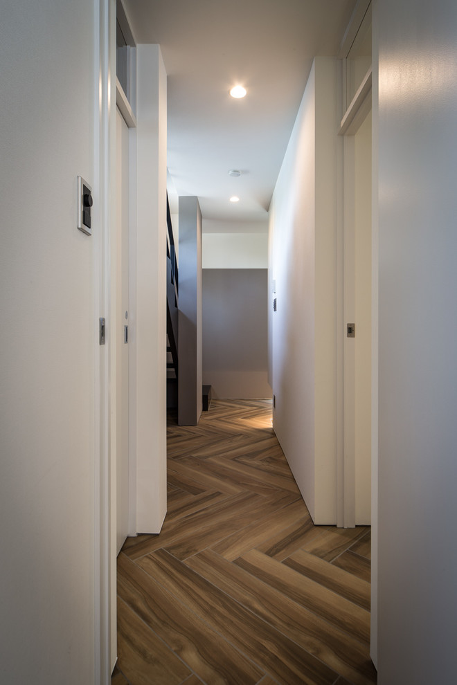 Пример оригинального дизайна: коридор в стиле модернизм с белыми стенами, паркетным полом среднего тона и коричневым полом