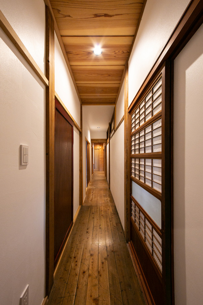 Cette photo montre un couloir tendance de taille moyenne avec un mur blanc, un sol en bois brun, un sol beige et poutres apparentes.
