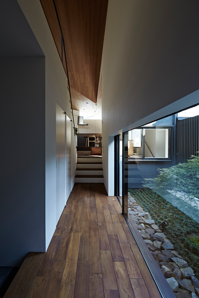 Réalisation d'un couloir minimaliste avec un mur blanc, un sol en bois brun et un sol marron.