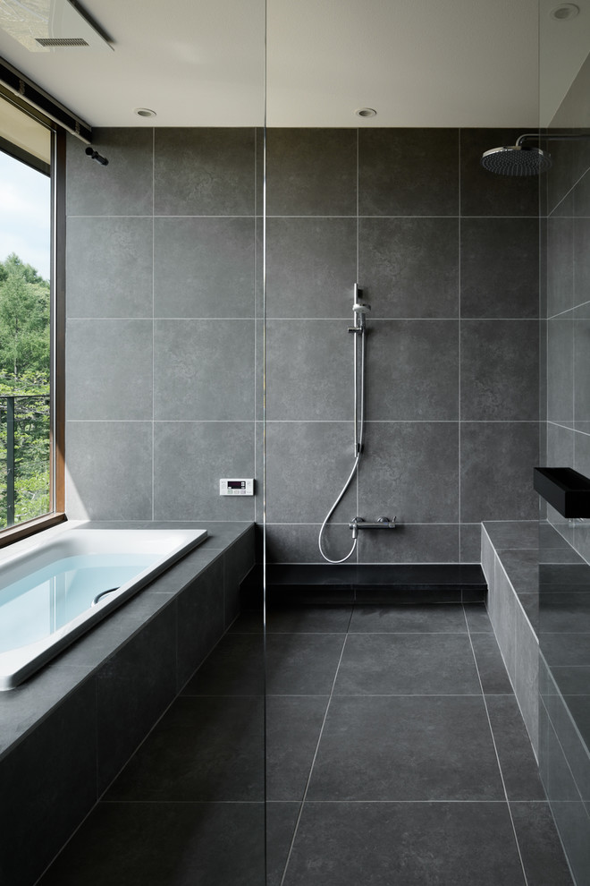 Modern inredning av ett badrum, med ett hörnbadkar, grå väggar, grått golv och med dusch som är öppen