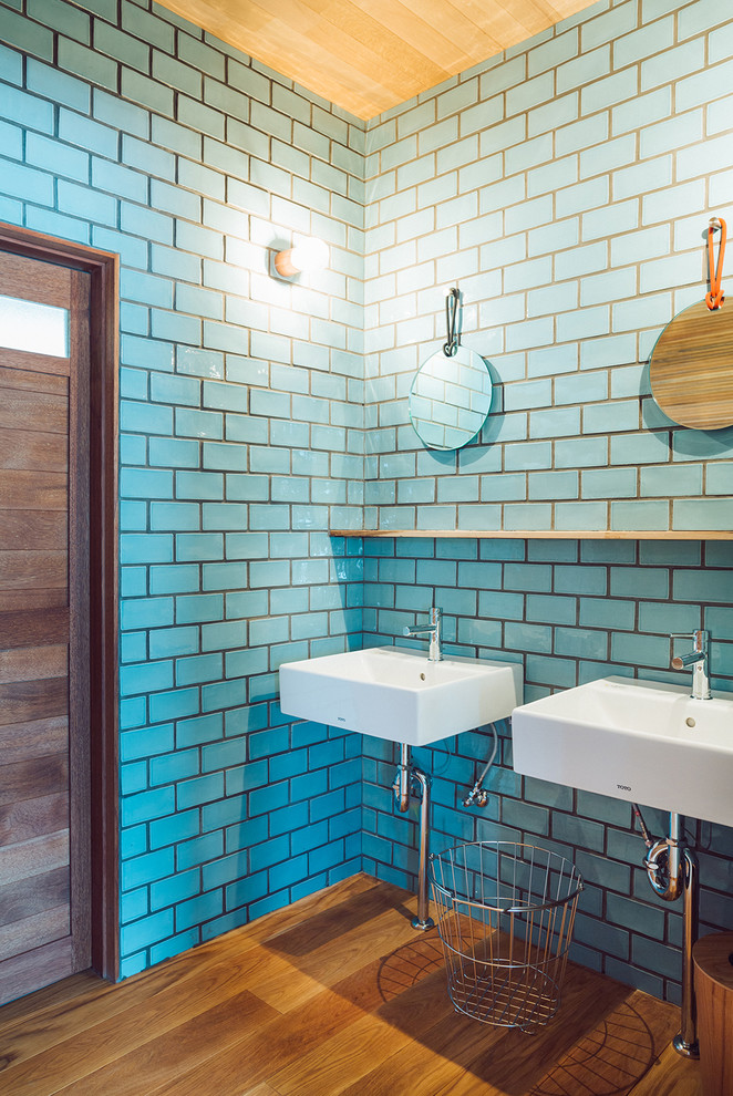 Modernes Badezimmer mit blauen Fliesen, Metrofliesen, Wandwaschbecken, blauer Wandfarbe und braunem Holzboden in Sonstige
