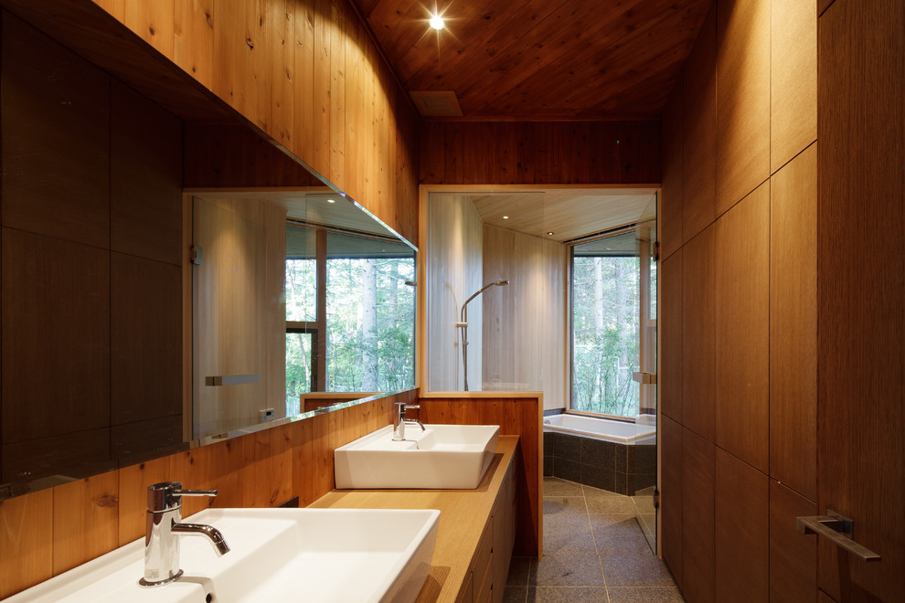 Aménagement d'une salle de bain asiatique en bois brun avec un placard à porte plane, un carrelage gris, un mur marron, une vasque, un plan de toilette en bois et un plan de toilette marron.