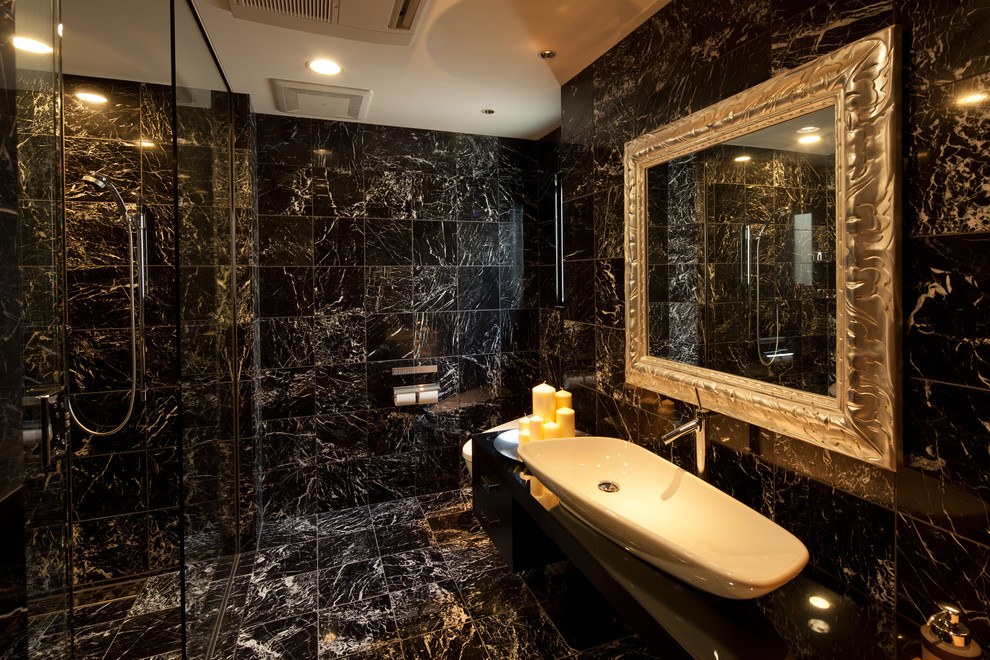 Modelo de cuarto de baño principal actual con ducha a ras de suelo, sanitario de una pieza, baldosas y/o azulejos negros, paredes negras, lavabo sobreencimera, suelo de mármol y encimeras negras
