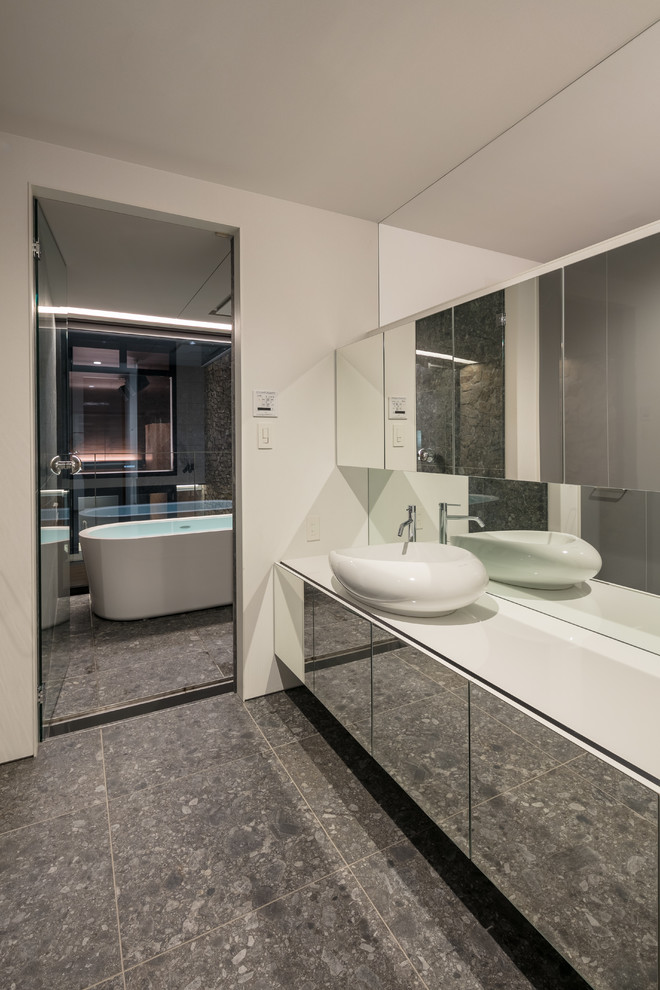 Contemporary bathroom in Kobe with flat-panel cabinets, white walls, a vessel sink, grey floors, a freestanding bath and white worktops.