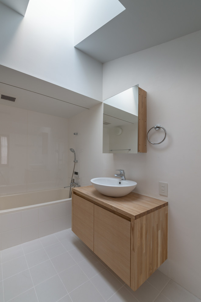 Cette image montre une salle de bain minimaliste en bois clair avec un placard à porte plane, un carrelage blanc, un mur blanc, une vasque et un plan de toilette en bois.