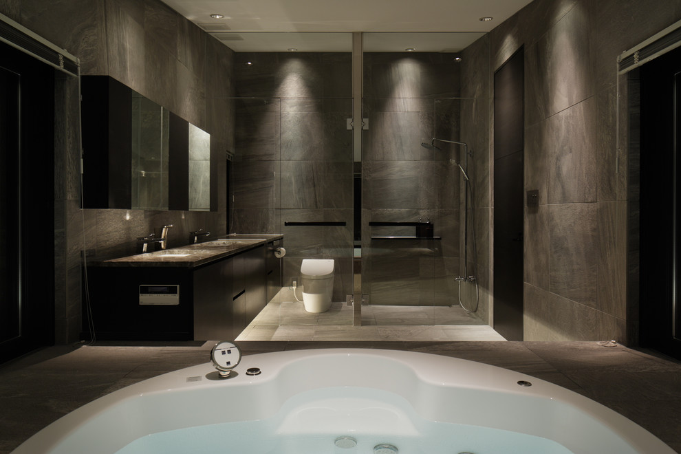Immagine di una stanza da bagno minimal con ante lisce, ante nere, vasca idromassaggio, WC monopezzo, pareti grigie e lavabo sottopiano