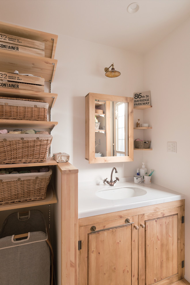 Idées déco pour une salle de bain campagne en bois clair avec un placard à porte plane, un carrelage blanc, un mur blanc et un lavabo encastré.