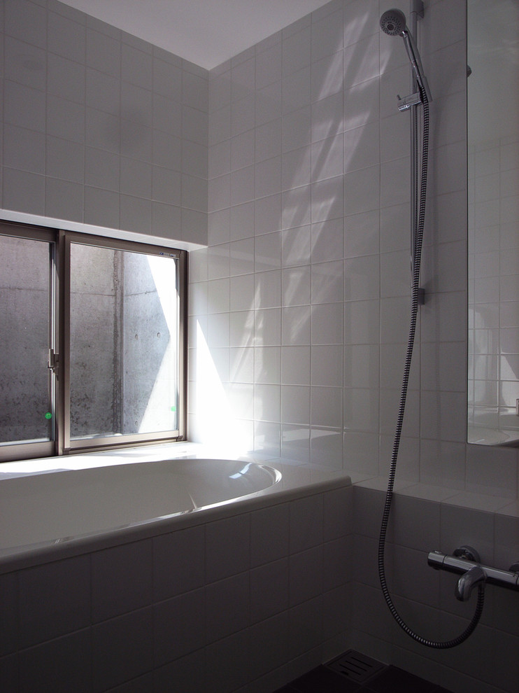 Cette photo montre une salle de bain moderne avec un placard à porte plane, des portes de placard blanches, un bain japonais, un espace douche bain, un bidet, un carrelage gris, des carreaux de porcelaine, un mur blanc, un sol en carrelage de porcelaine, un lavabo intégré et un plan de toilette en surface solide.