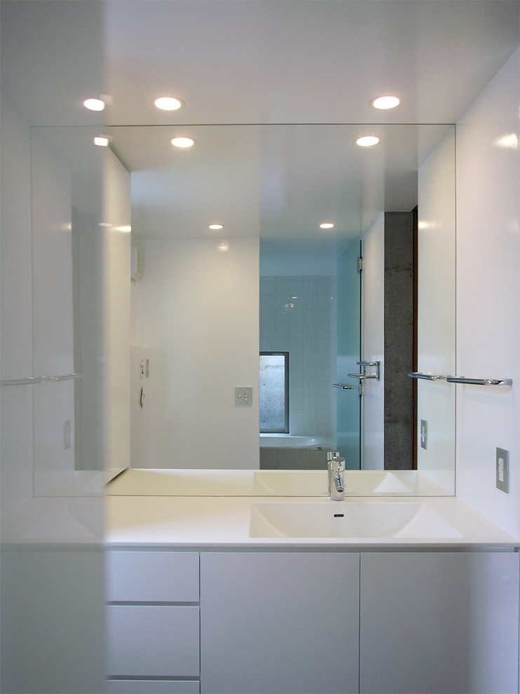 Cette image montre une salle de bain minimaliste avec un bain japonais, un espace douche bain, un bidet, un mur blanc, un sol en carrelage de porcelaine, un lavabo intégré et un plan de toilette en surface solide.