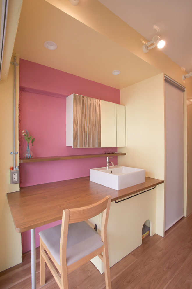 Aménagement d'une salle de bain asiatique avec un sol en bois brun, une vasque, un plan de toilette en bois et un mur rose.