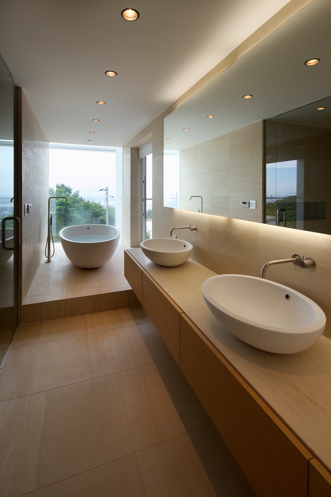 Пример оригинального дизайна: главная ванная комната в стиле модернизм с плоскими фасадами, светлыми деревянными фасадами, отдельно стоящей ванной, бежевыми стенами, настольной раковиной, столешницей из дерева и бежевой столешницей