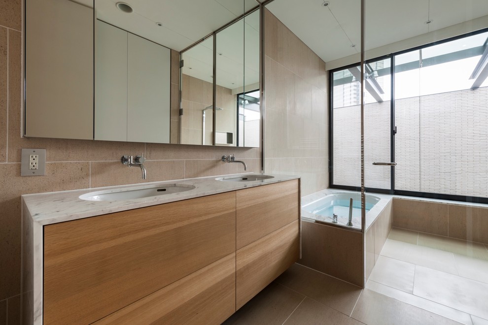 Свежая идея для дизайна: главная ванная комната в стиле модернизм с плоскими фасадами, светлыми деревянными фасадами, ванной в нише, бежевой плиткой, бежевыми стенами и врезной раковиной - отличное фото интерьера