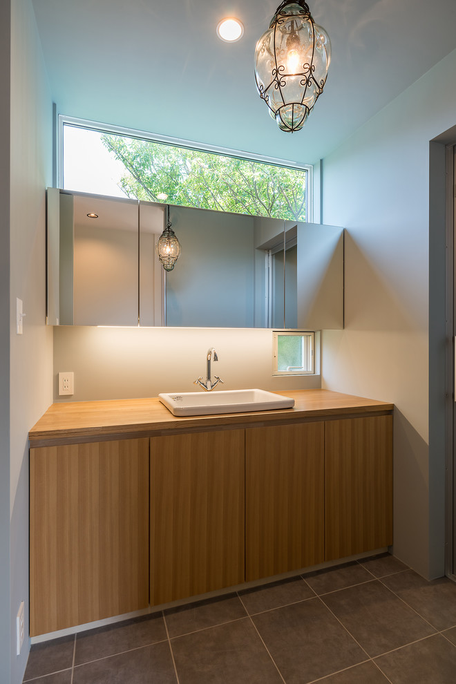 Modernes Badezimmer mit flächenbündigen Schrankfronten, hellbraunen Holzschränken, weißer Wandfarbe, Waschtisch aus Holz, grauem Boden und brauner Waschtischplatte in Sonstige