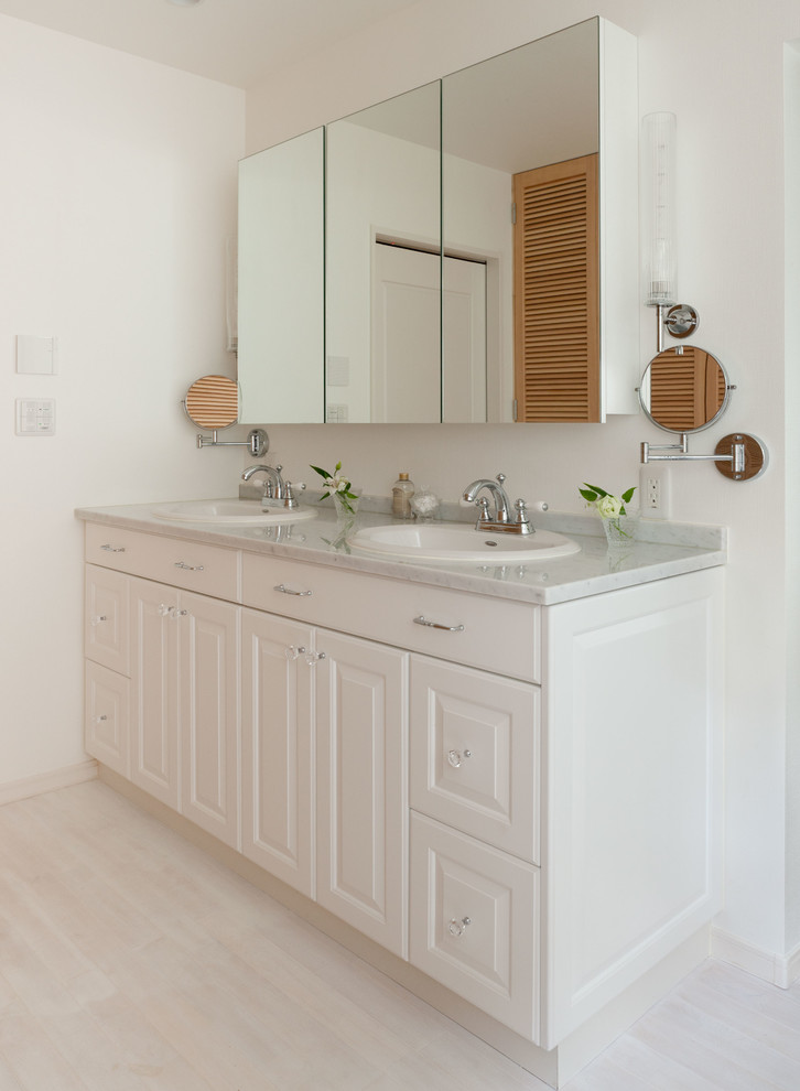 Inredning av ett mellanstort badrum, med luckor med glaspanel, spegel istället för kakel, vita väggar, ljust trägolv, ett nedsänkt handfat och bänkskiva i kvarts