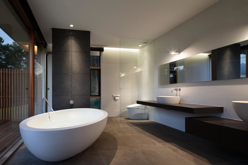 Bild på ett funkis badrum, med ett fristående badkar, vita väggar, ett fristående handfat, träbänkskiva och en toalettstol med hel cisternkåpa