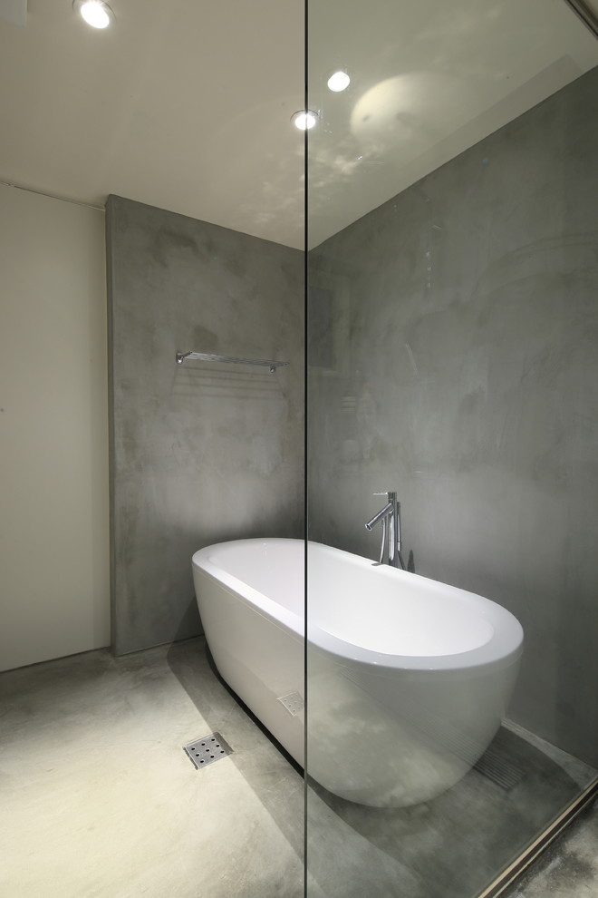 Modelo de cuarto de baño moderno con bañera exenta, paredes grises y suelo de cemento