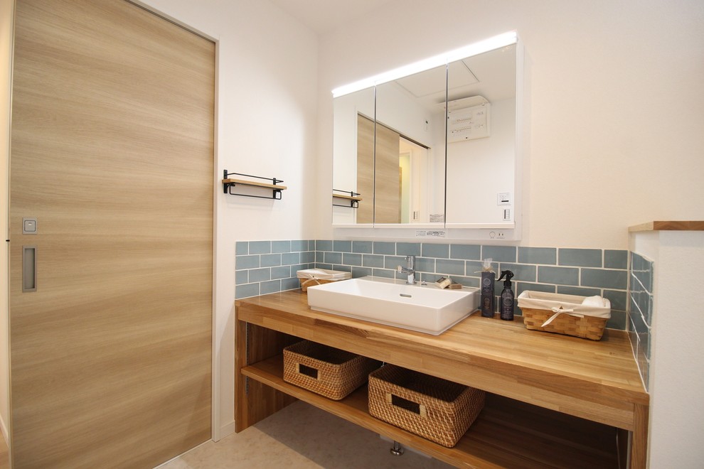 Photo of a world-inspired bathroom in Osaka with open cabinets, medium wood cabinets, blue tiles, metro tiles, white walls, a vessel sink, wooden worktops, beige floors and brown worktops.