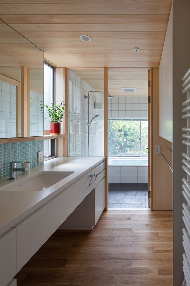 Aménagement d'une salle de bain asiatique avec un placard à porte plane, des portes de placard blanches, un carrelage bleu, un sol en bois brun, un lavabo intégré et un sol marron.