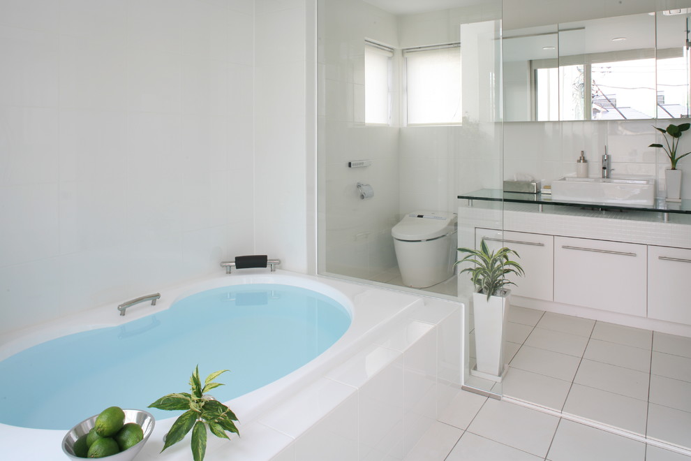 Réalisation d'une salle de bain principale minimaliste avec une vasque, des portes de placard blanches, une baignoire posée, WC à poser, un mur blanc et un plan de toilette en verre.