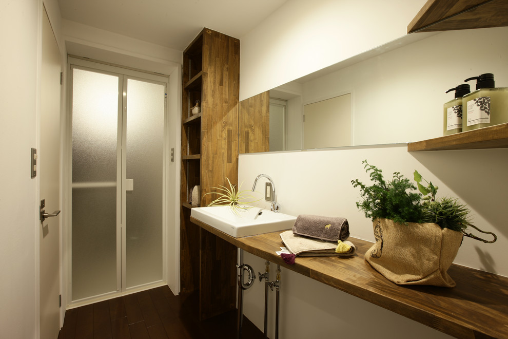 Modelo de cuarto de baño escandinavo con paredes blancas, suelo de madera oscura, lavabo tipo consola, suelo marrón, encimera de madera y encimeras marrones