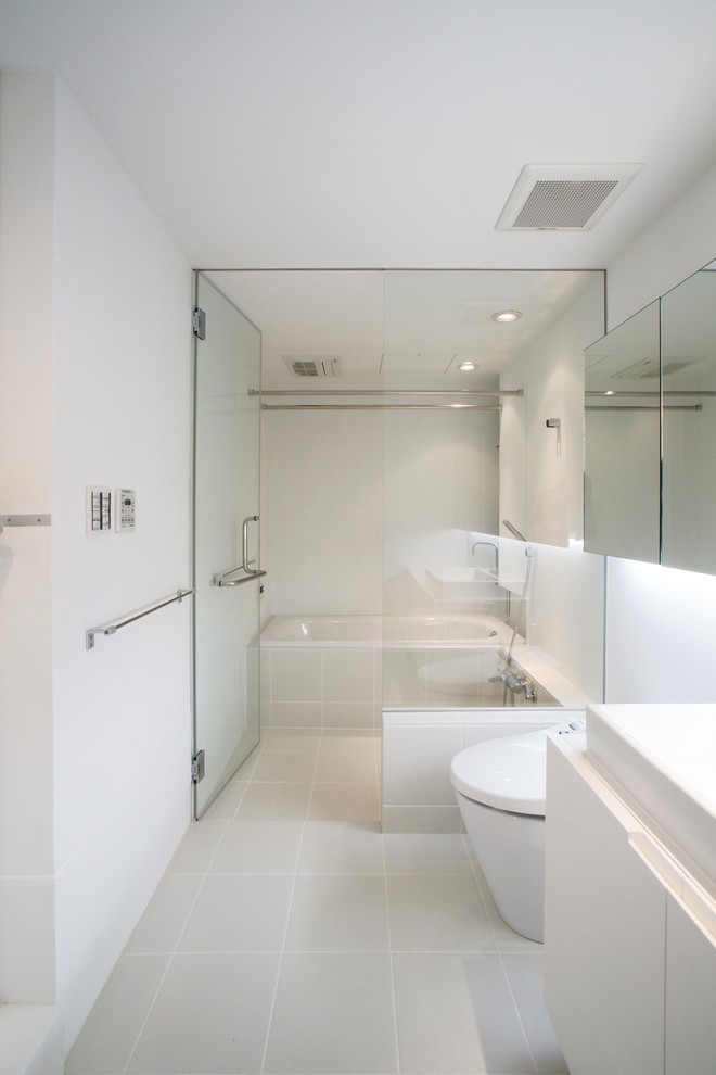 東京23区にある中くらいなコンテンポラリースタイルのおしゃれなマスターバスルーム (ガラス扉のキャビネット、白いキャビネット、ドロップイン型浴槽、洗い場付きシャワー、一体型トイレ	、白いタイル、白い壁、セラミックタイルの床、グレーの床、白い洗面カウンター) の写真