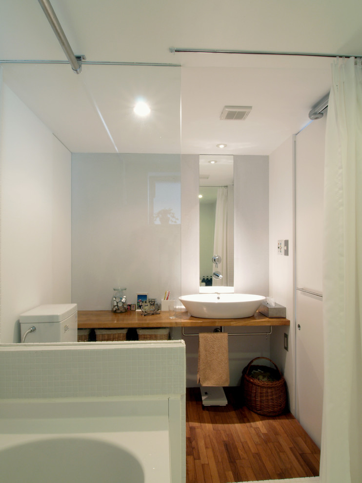 Exempel på ett litet modernt en-suite badrum, med öppna hyllor, skåp i mellenmörkt trä, träbänkskiva, ett hörnbadkar, en öppen dusch, en toalettstol med separat cisternkåpa, vita väggar, mellanmörkt trägolv och ett fristående handfat