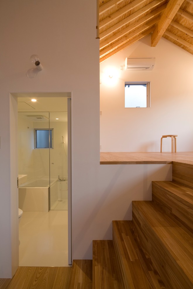 Cette image montre une petite salle de bain minimaliste avec un placard à porte plane, des portes de placard blanches, un espace douche bain, WC à poser, un mur blanc, une vasque et aucune cabine.