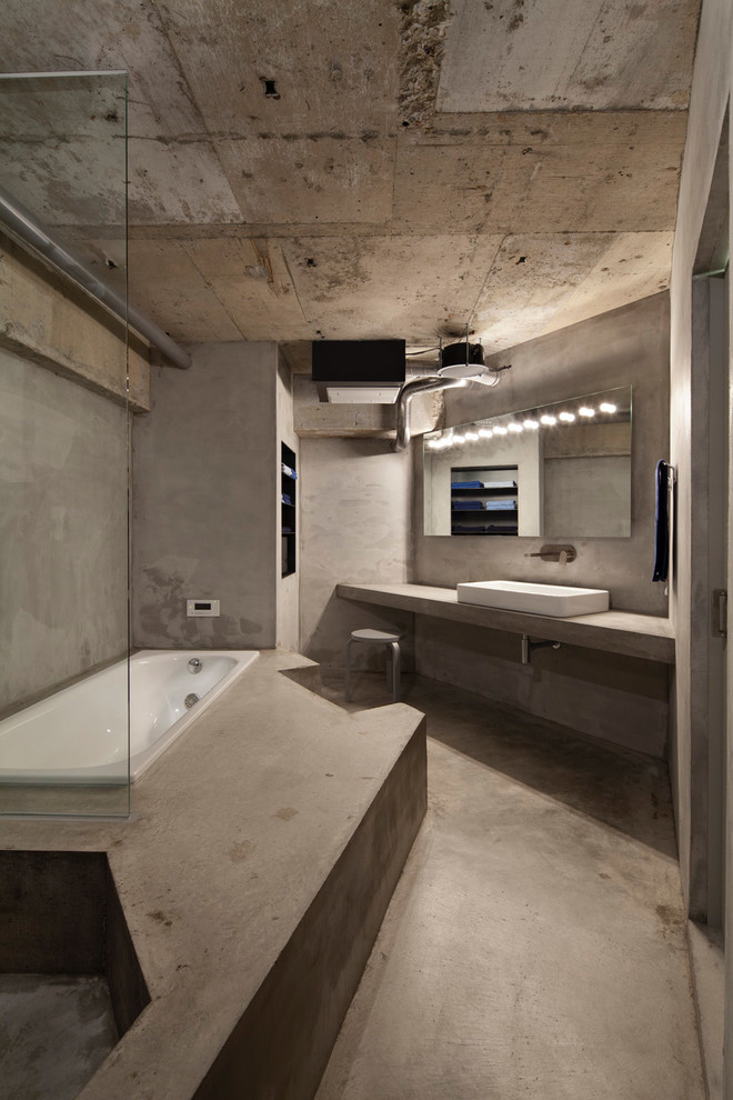 Industriell inredning av ett badrum, med ett platsbyggt badkar, grå väggar, betonggolv och grått golv