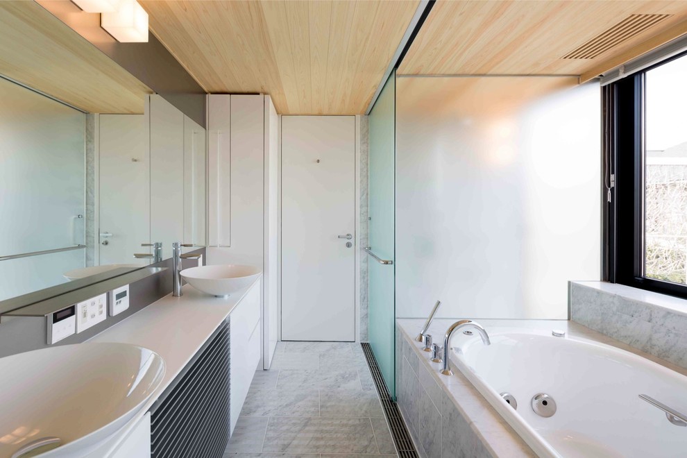 Imagen de cuarto de baño actual con armarios con paneles lisos, puertas de armario blancas, bañera esquinera, paredes blancas, lavabo sobreencimera y suelo gris