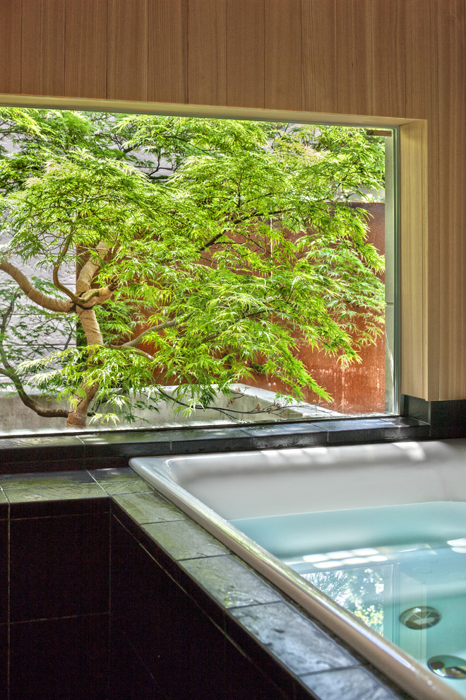 東京23区にあるアジアンスタイルのおしゃれなお風呂の窓 (ドロップイン型浴槽、黒いタイル、茶色い壁) の写真