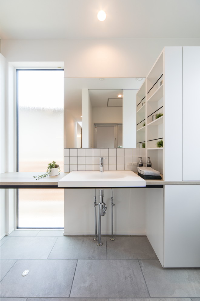 Foto på ett minimalistiskt badrum, med öppna hyllor, vita skåp, vit kakel, vita väggar, betonggolv, ett fristående handfat och grått golv