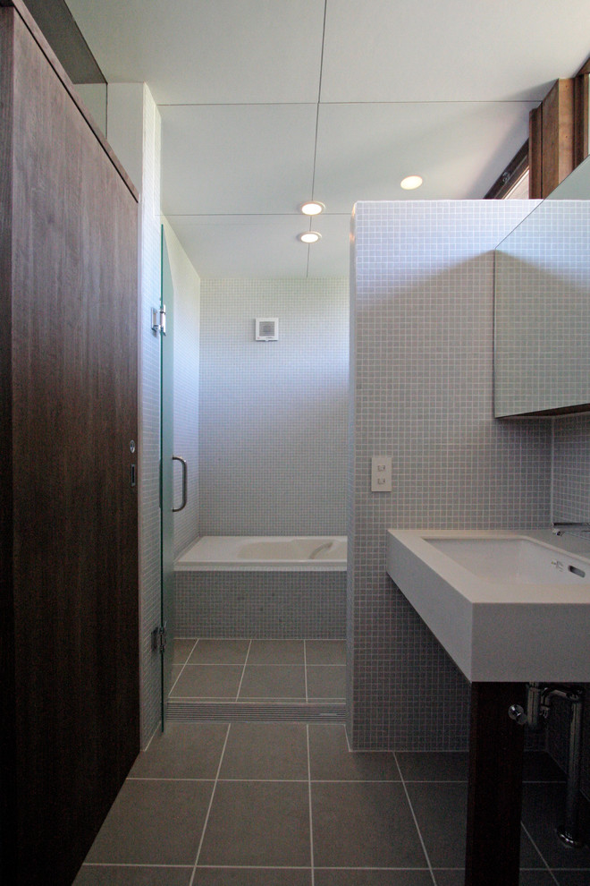 Cette photo montre une salle de bain moderne avec un placard à porte plane, des portes de placard marrons, WC séparés, mosaïque, un mur gris, un lavabo suspendu, un sol en carrelage de porcelaine, un plan de toilette en surface solide et un sol gris.