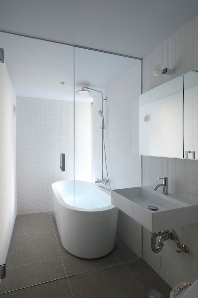 Стильный дизайн: маленькая ванная комната со стиральной машиной в стиле модернизм с стеклянными фасадами, белыми фасадами, отдельно стоящей ванной, двойным душем, унитазом-моноблоком, белой плиткой, плиткой мозаикой, белыми стенами, полом из керамогранита, подвесной раковиной, серым полом, душем с распашными дверями, белой столешницей, тумбой под одну раковину, напольной тумбой, потолком с обоями и обоями на стенах для на участке и в саду - последний тренд