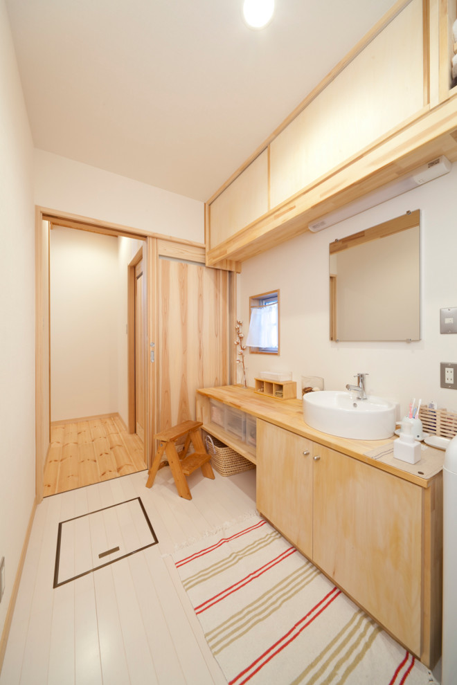 Foto de cuarto de baño de estilo zen con paredes blancas, suelo blanco, armarios con paneles lisos, puertas de armario de madera clara, lavabo sobreencimera, encimera de madera y encimeras beige