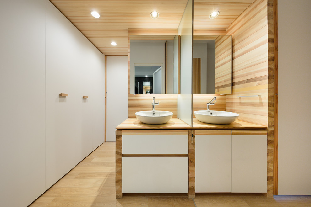 Idéer för att renovera ett minimalistiskt beige beige badrum, med träbänkskiva, vita skåp, vita väggar, ljust trägolv, ett fristående handfat och beiget golv