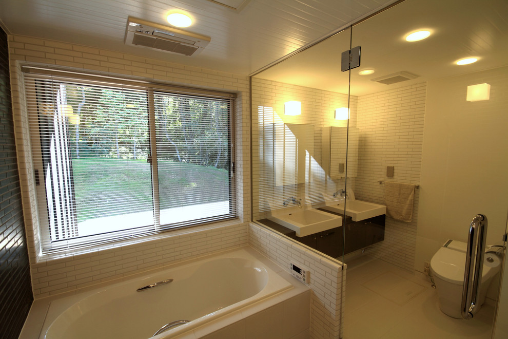 他の地域にあるモダンスタイルのおしゃれな浴室 (ドロップイン型浴槽、白いタイル、磁器タイル、白い壁、磁器タイルの床、白い床) の写真