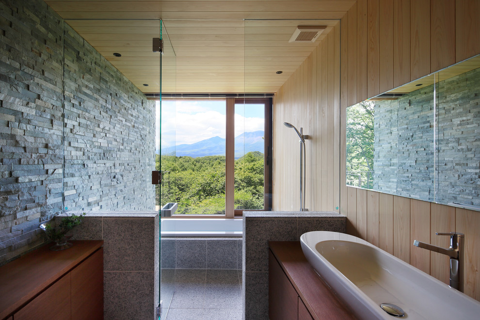 他の地域にあるコンテンポラリースタイルのおしゃれな浴室 (フラットパネル扉のキャビネット、中間色木目調キャビネット、和式浴槽、グレーの壁、ベッセル式洗面器、開き戸のシャワー) の写真