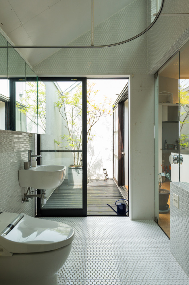 Foto på ett funkis badrum, med en toalettstol med hel cisternkåpa, vit kakel, mosaik, vita väggar, mosaikgolv och ett väggmonterat handfat