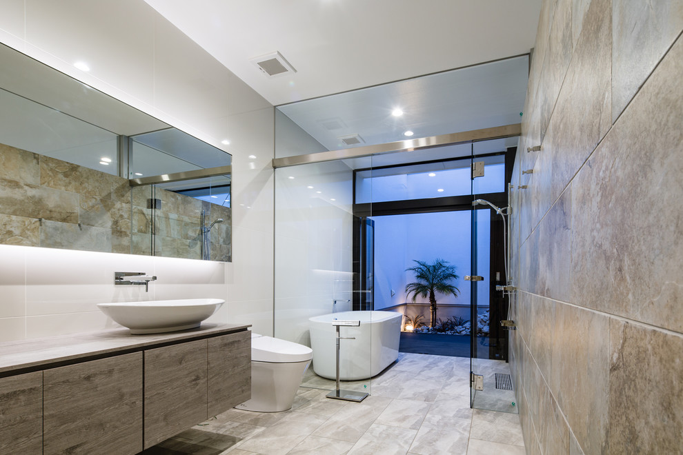 Стильный дизайн: главная ванная комната в современном стиле с плоскими фасадами, серыми фасадами, отдельно стоящей ванной, душевой комнатой, унитазом-моноблоком, бежевой плиткой, серыми стенами, настольной раковиной, серым полом, открытым душем и бежевой столешницей - последний тренд