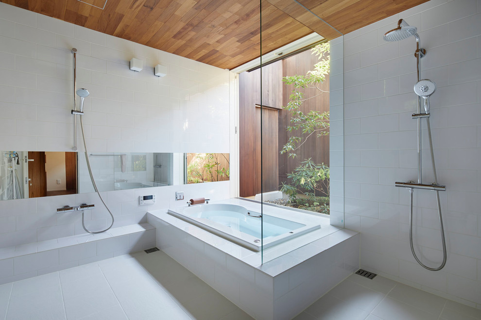 Asiatisk inredning av ett badrum, med ett platsbyggt badkar, en dubbeldusch, vit kakel, vitt golv och med dusch som är öppen