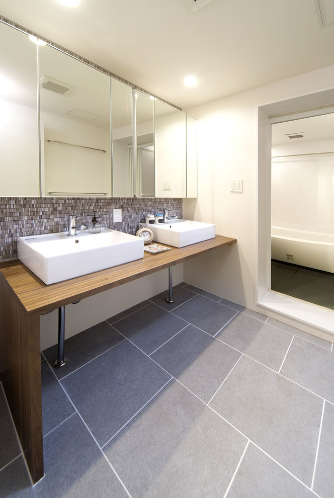 Immagine di una stanza da bagno etnica con ante lisce, pareti bianche, lavabo a bacinella, pavimento con piastrelle in ceramica, top in legno, piastrelle a mosaico e top marrone
