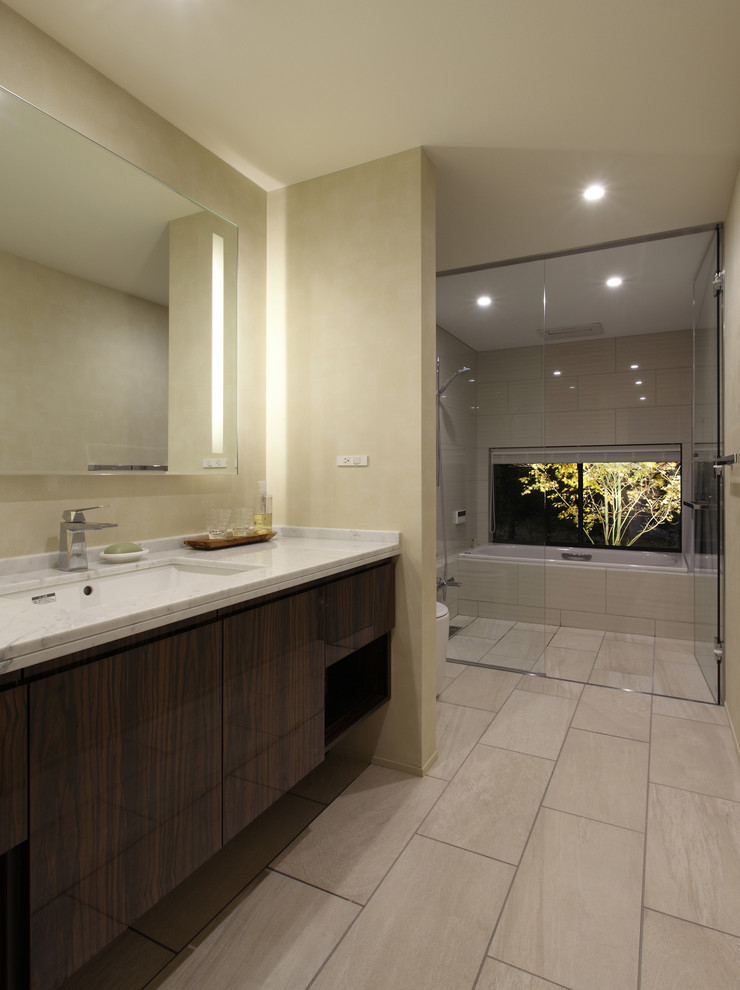 Idées déco pour une salle de bain principale moderne avec un placard à porte plane, des portes de placard marrons, WC à poser, un carrelage beige, un mur beige, un sol en carrelage de porcelaine, un lavabo encastré, un plan de toilette en surface solide, un sol beige et un plan de toilette blanc.