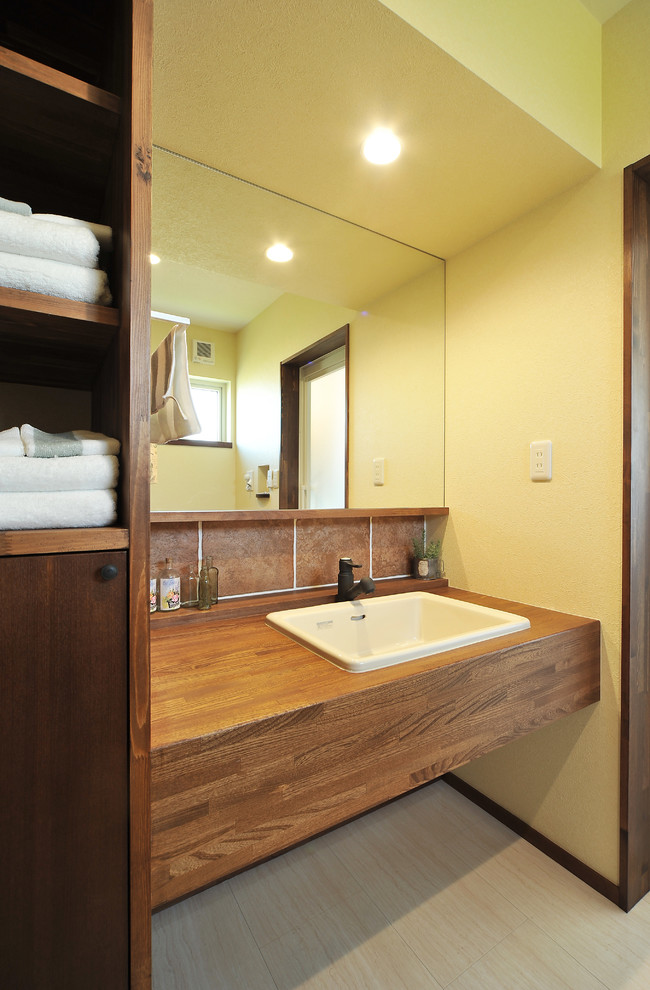 Ejemplo de cuarto de baño de estilo zen con armarios abiertos, paredes amarillas, lavabo encastrado y suelo beige