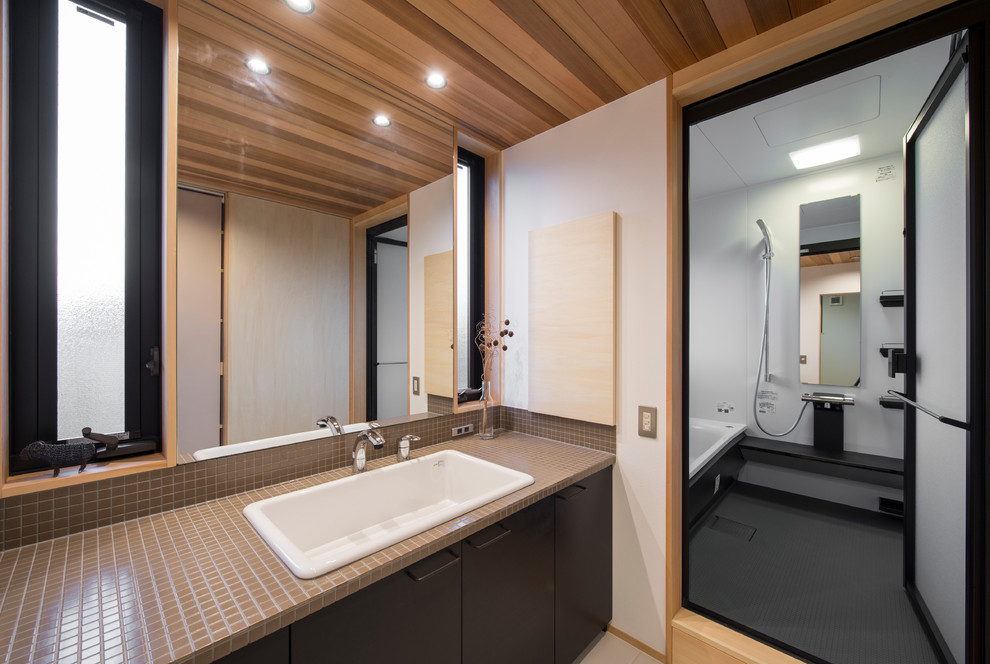 Imagen de cuarto de baño asiático con armarios con paneles lisos, puertas de armario de madera en tonos medios, paredes blancas, lavabo encastrado y encimera de azulejos