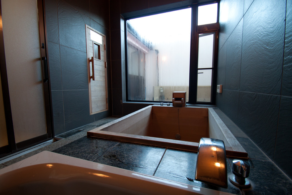 Inredning av ett asiatiskt badrum, med ett japanskt badkar, svarta väggar och marmorgolv