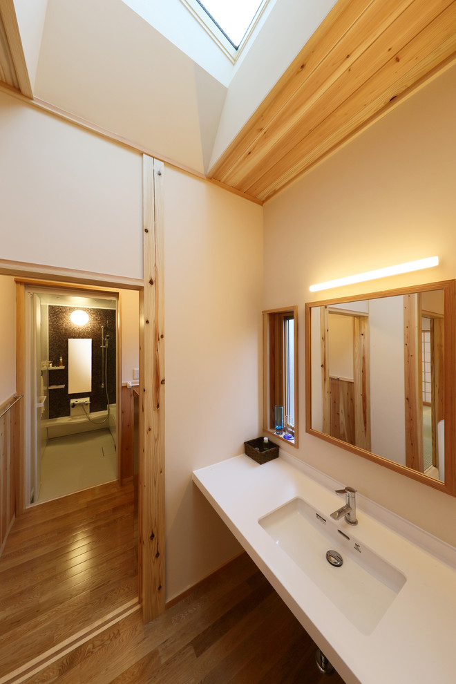 Aménagement d'une salle de bain scandinave avec un mur blanc, un sol en bois brun, un lavabo intégré et un plan de toilette blanc.