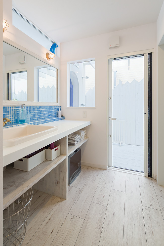 Ejemplo de cuarto de baño costero con armarios abiertos, puertas de armario de madera clara, baldosas y/o azulejos azules, baldosas y/o azulejos en mosaico, paredes blancas, lavabo encastrado, suelo beige y encimeras blancas